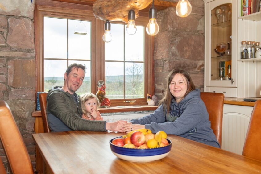 Kayleigh, pictured with her husband Jamie and daughter Bella at the wooden kitchen table.