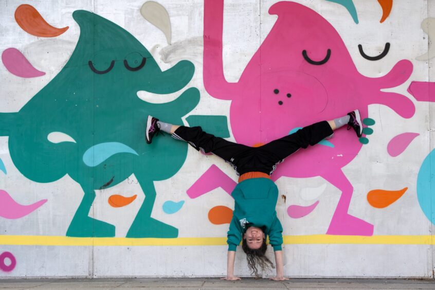 Sofia Kondylia does a handstand against a wall with a colourful mural on it