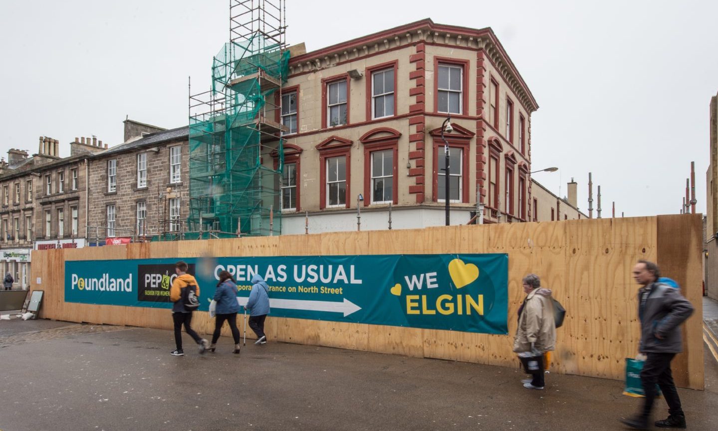 Poundland building behind "we love Elgin" boarding. 