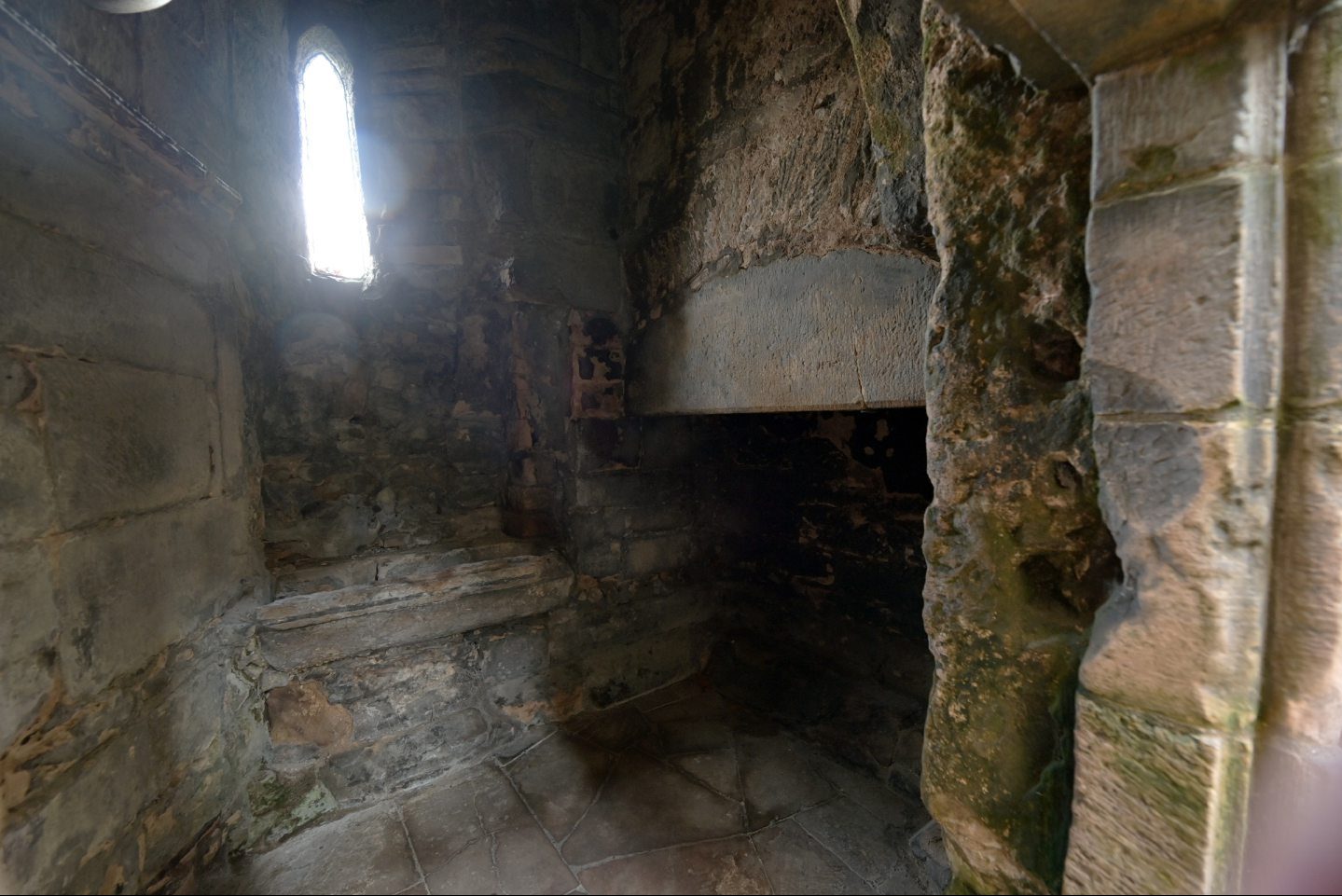 Dark stone room inside Elgin Cathedral with fireplace and narrow window 