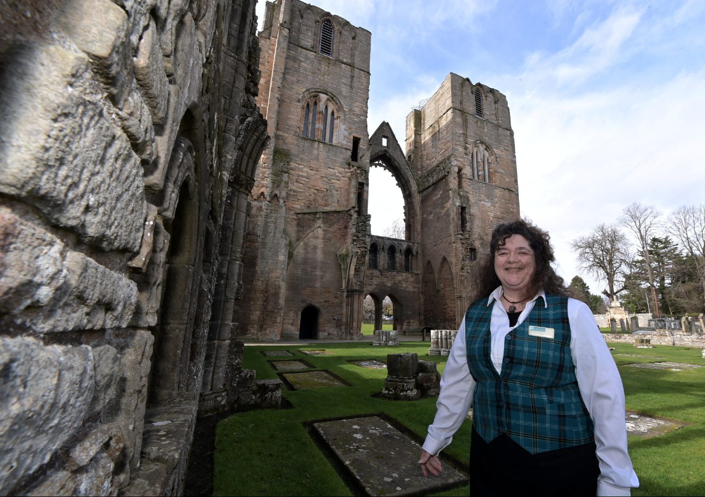 Historic Scotland guide in uniform with Elgin Cathedral ruins behind. 