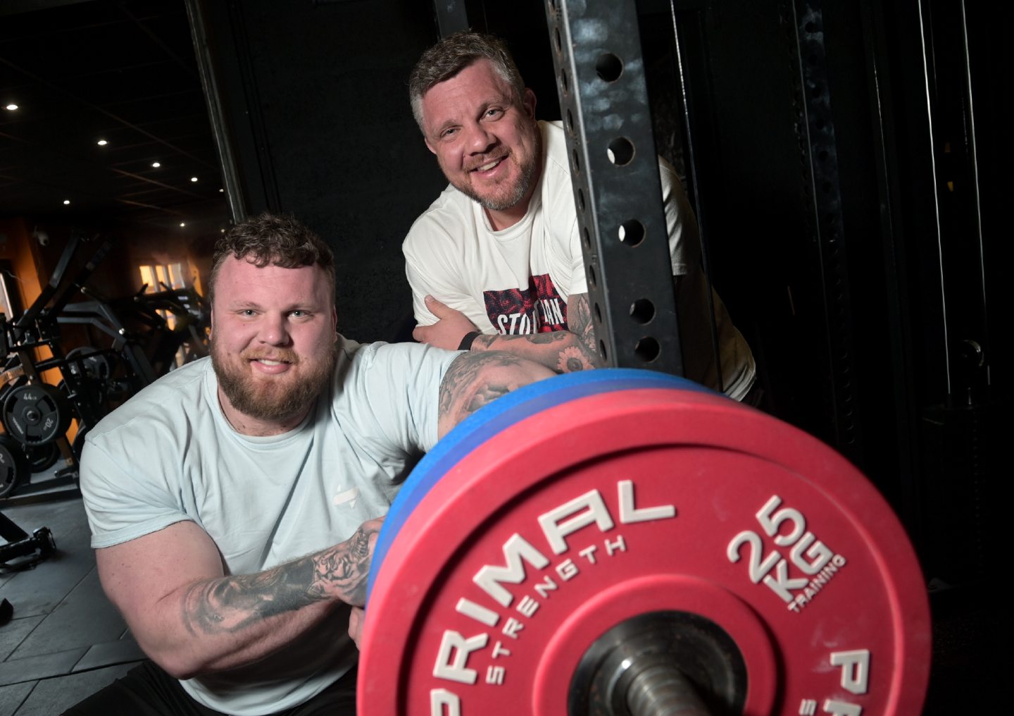 Tom and Luke Stoltman smiling holding weights. 