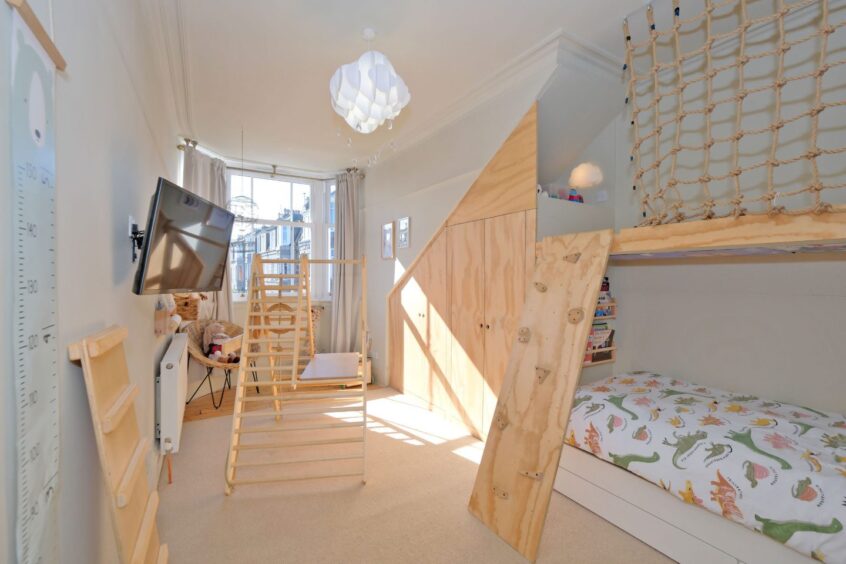 A child's bedroom in the renovated home in Aberdeen with light wood-toned furniture. There is a small climbing frame in the middle of the room, a small wall-mounted TV and a climbing ladder to a nook above the bed