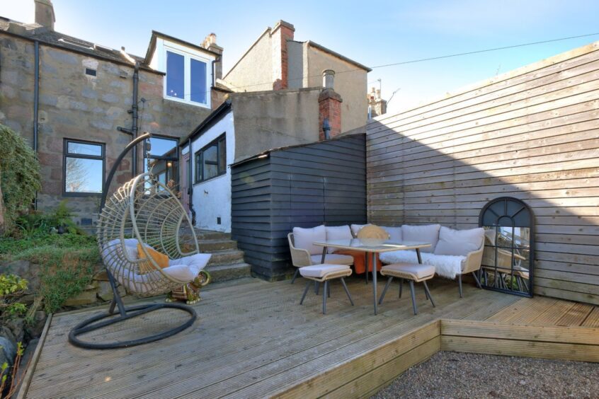 The patio in the garden of the renovated home in Aberdeen with a wooden decked area. There's patio furniture including a hanging chair and coffee table and chairs