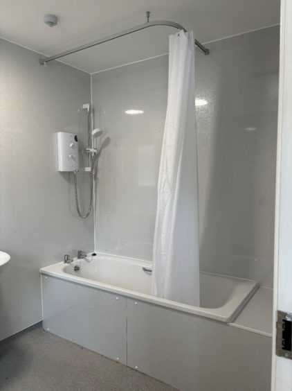 A white tiled bathroom with bath and white shower curtain.