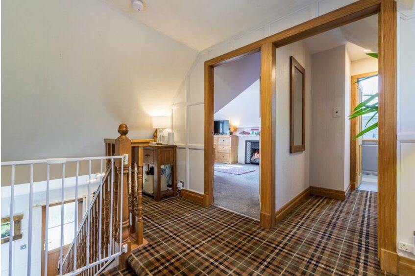 The wooden stairs and wooden door frames compliment the tartan carpet. 