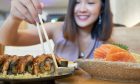 Asian woman holding a sushi with chopsticks to eat.