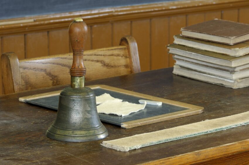 A school desk from the 1920s, showing the bell, a slate with chalk, and a strap for punishment.