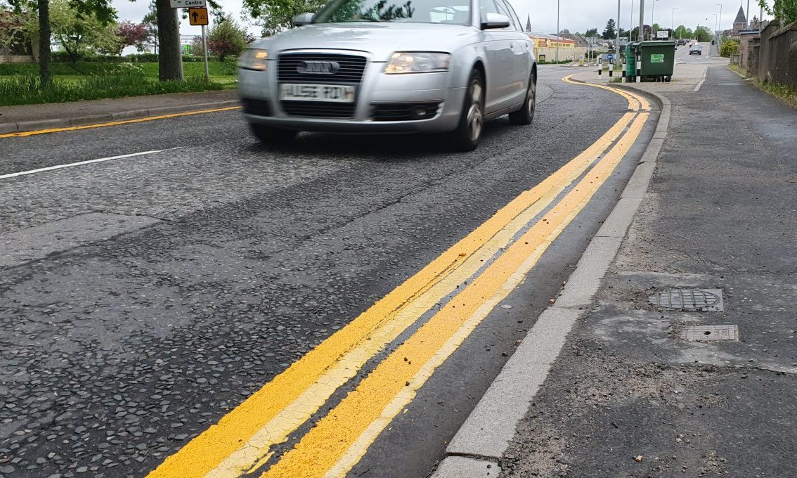 Silver car driving past double yellow lines. 