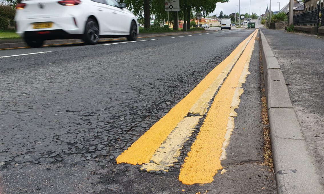 White car driving past double yellow lines. 