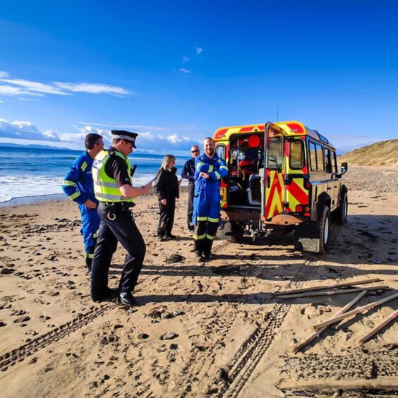 Coastguard teams, police and inspectors on Machrihanish beach amidst blue skies 
