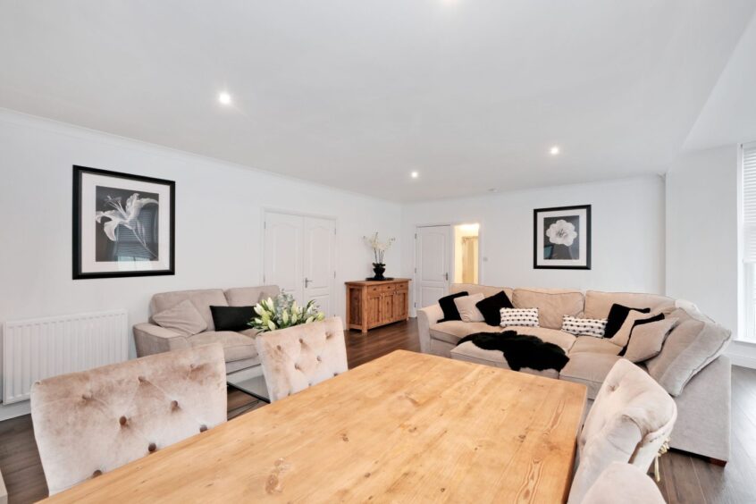 The living/dining area in the home with plush cream sofas and dining chairs