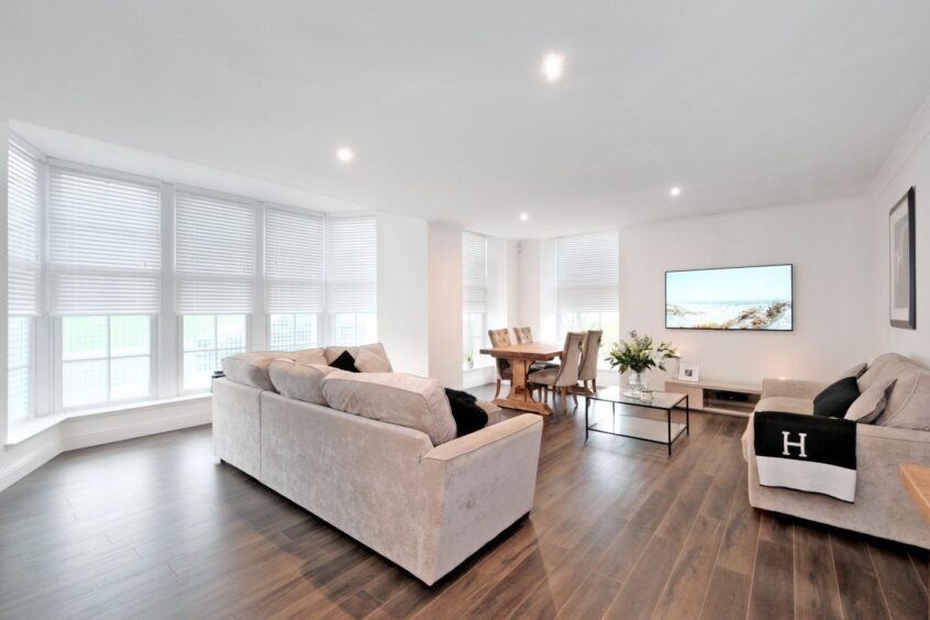 The living room in the home with white walls, lots of windows and dark wooden floors.