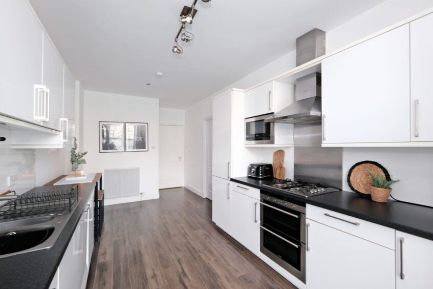 The kitchen has white cupboards, black countertops and dark wooden flooring