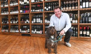 Graeme Hetherington with his dog Monty, pictured in front of shelves filled with bottles at the new wine shop and bar on Bon Accord Street.