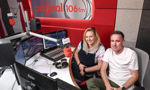 Claire Kinnaird and Pete McIntosh sitting at a radio desk with a red Original 106 background