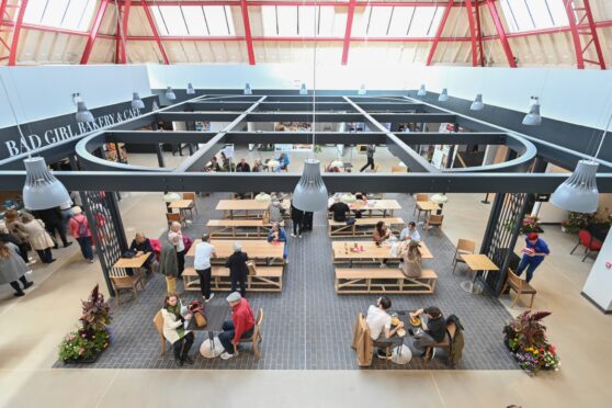 People sit and eat beneath a metal structure in the market's food hall.