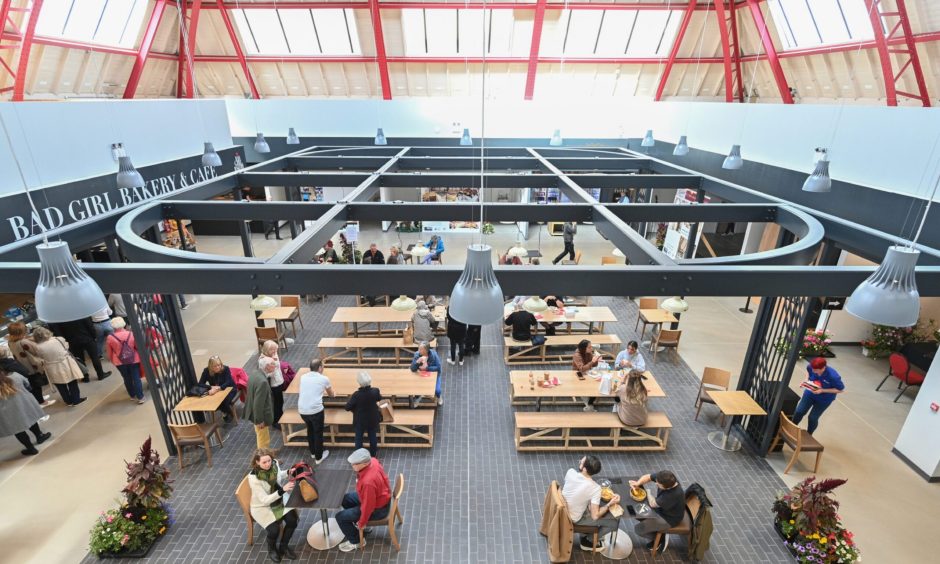 People sit and eat beneath a metal structure in the market's food hall.