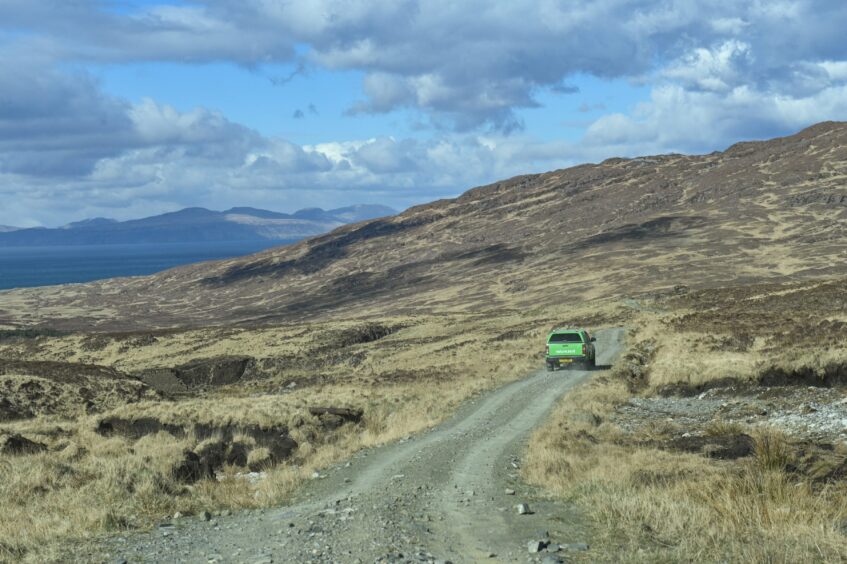 A car drives on a gravel road on the Isle of Rum.