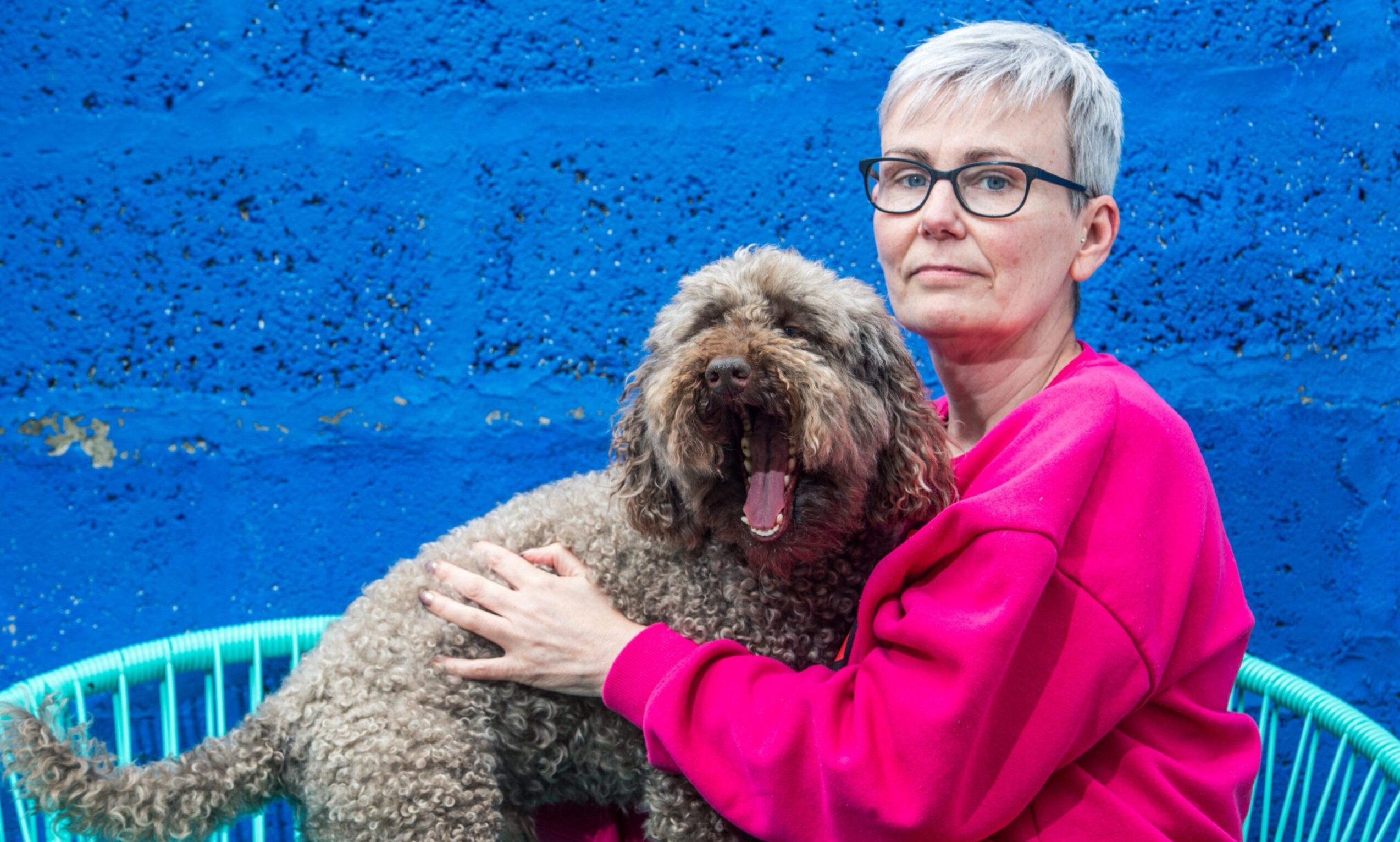 Jo Keown sitting on chair with arms round dog. 