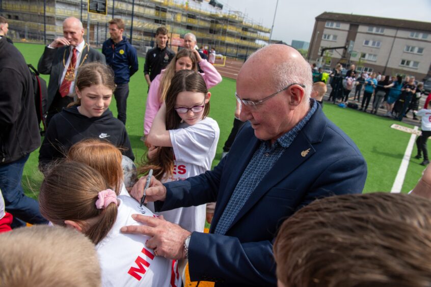 Don's legend Willie Miller surrounded by young school children as he signs football tops.