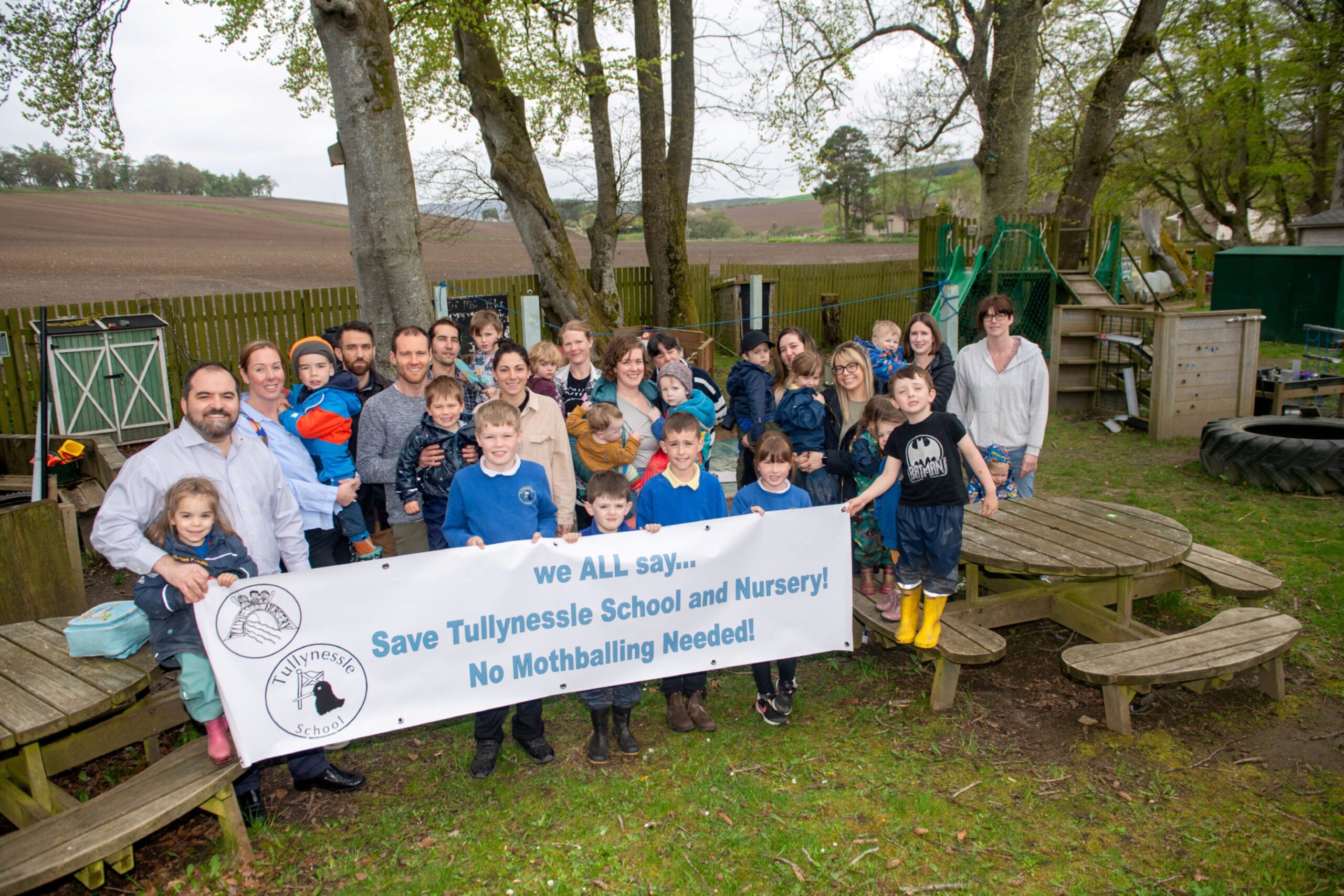 Children and parents holding up a banner reading "we ALL say... Save Tullynessle school and nursery! No mothballing needed!"