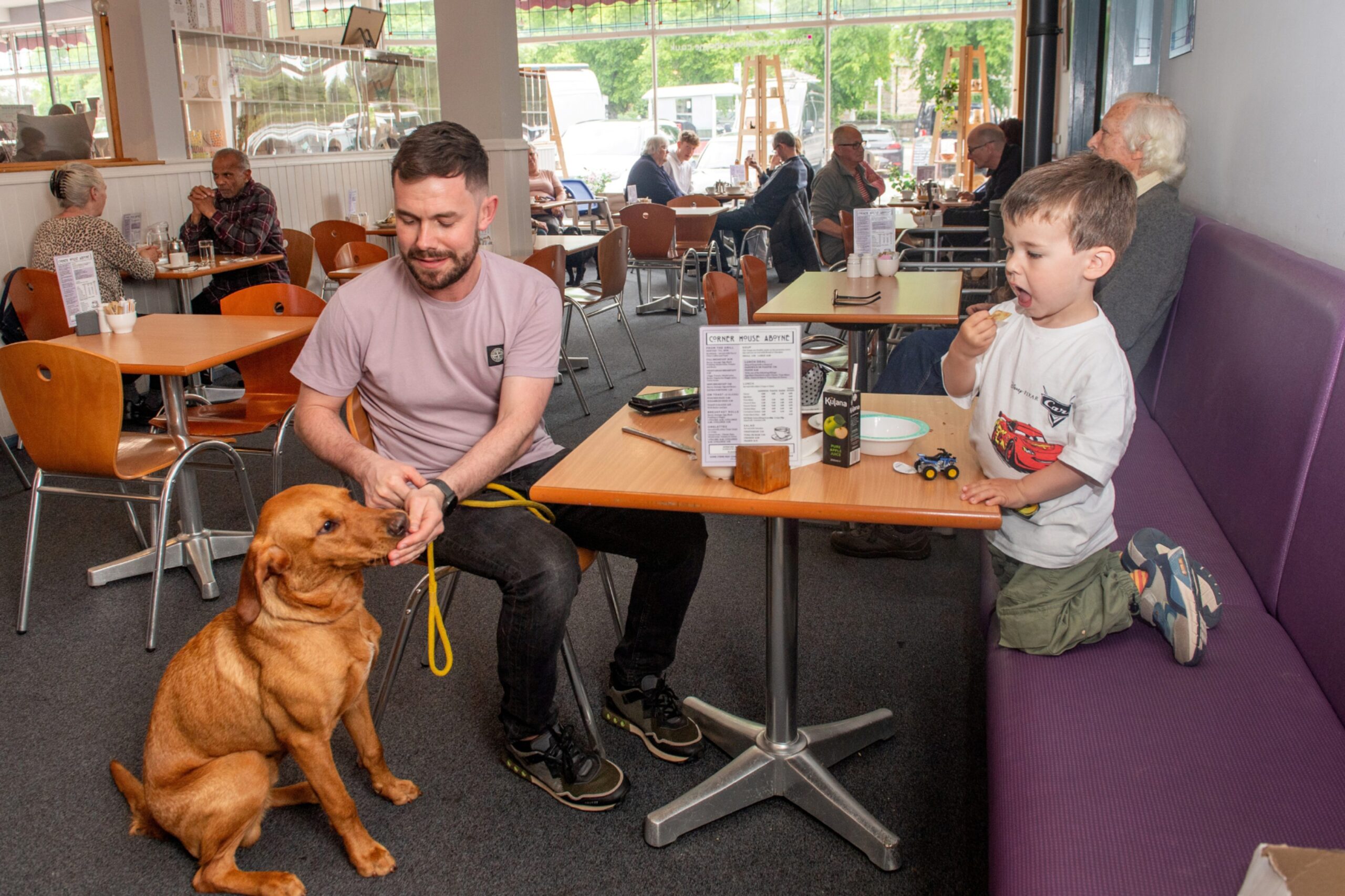 A man and young boy in the Aboyne tearoom with their dog