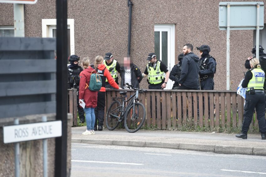 Blurred image of man being escorted from house by police in Inverness