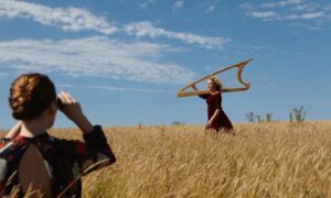 HOlding a harp, Ruth Wall runs through a field while being photographed.