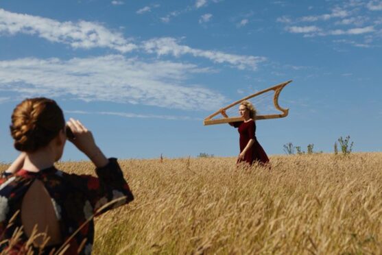 HOlding a harp, Ruth Wall runs through a field while being photographed.
