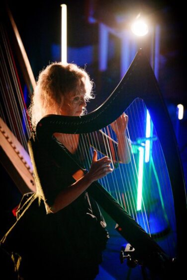Ruth Wall playing a harp on stage with a spectacular light show around her.
