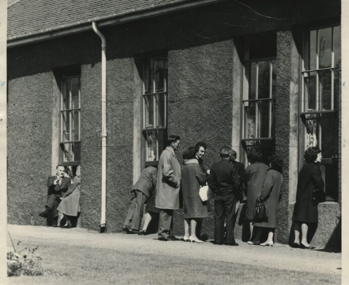 A line of people visiting their loved ones from the outside of the hospital. 