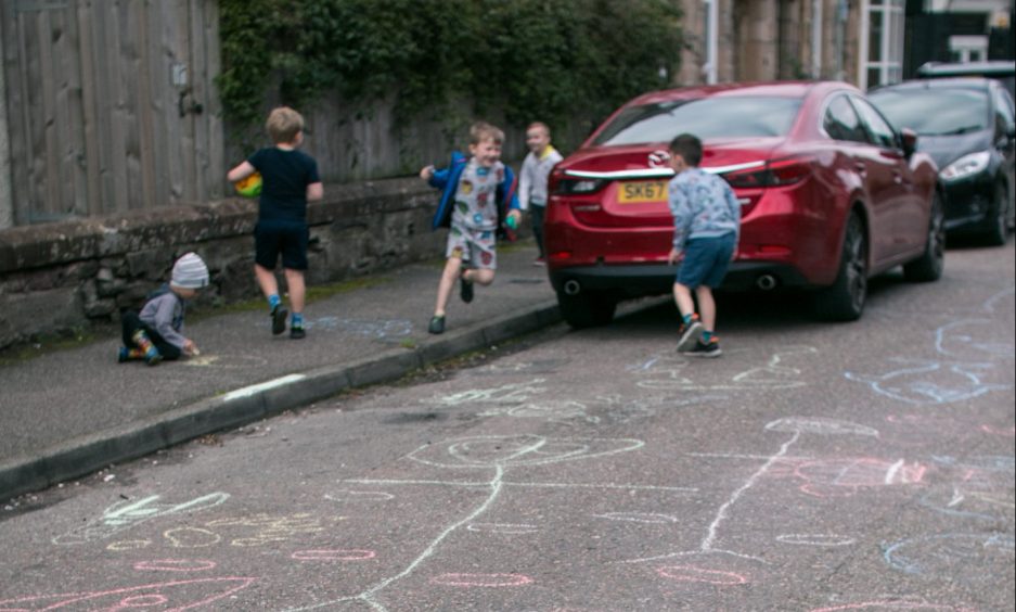 Children playing in the street with one drawing on the sidewalk in chalk.
