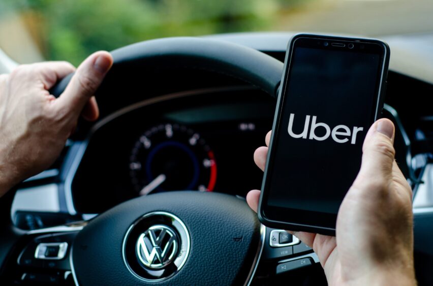 Person at the wheel of a Volkswagen holding a mobile attempting to open the Uber app.