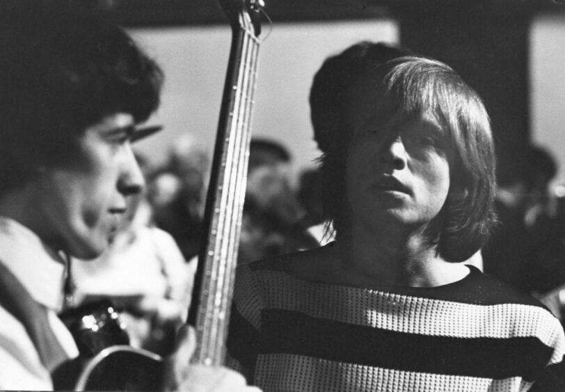 Bill Wyman holding a guitar, and Brian Jones, pictured in July 1964.
