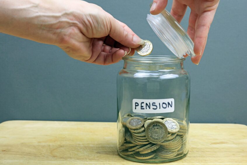 A hand putting pound coin into glass jar. 