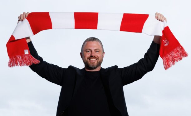 Aberdeen manager Jimmy Thelin raises a club scarf at Pittodrie.