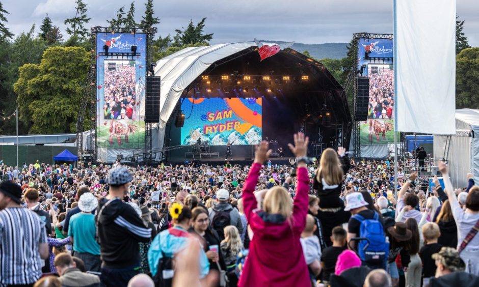 Crowds waving as they enjoy live music from the Belladrum festival main stage in the distance.