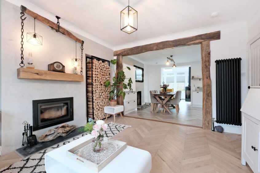 The open plan living room with a large archway to the dining area. The room is mainly white with rustic pale wood accents