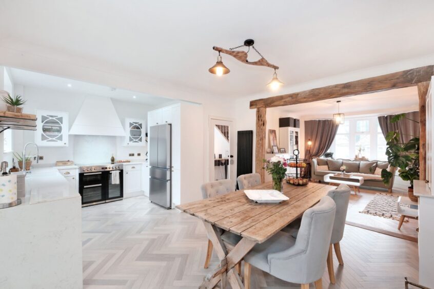 The dining area and kitchen with white walls, cupboards and countertops, pale herringbone flooring and rustic pale wood accents