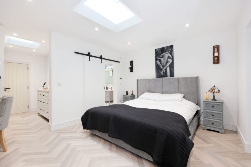 The bedroom in the Aberdeen home makeover with pale herringbone flooring, white walls and grey accents