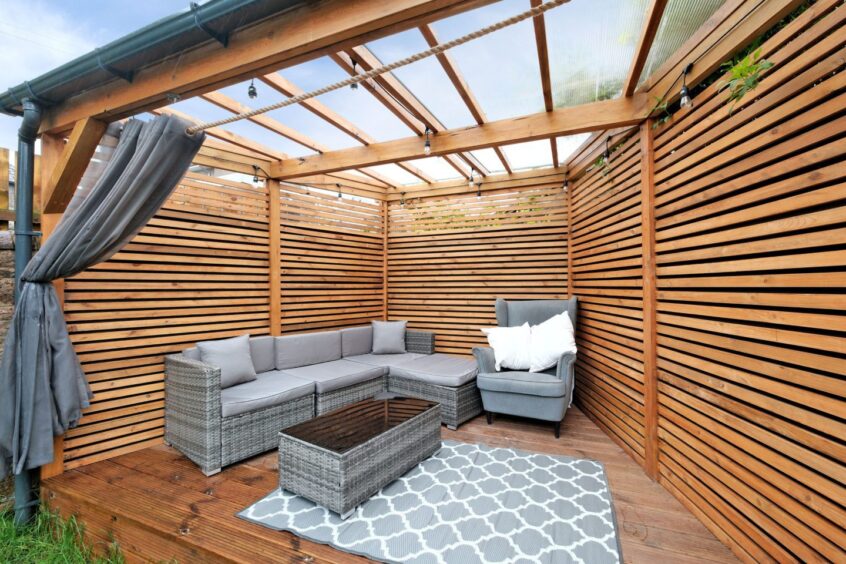 The wooden sheltered outdoor area, with grey patio furniture and a curtain for privacy