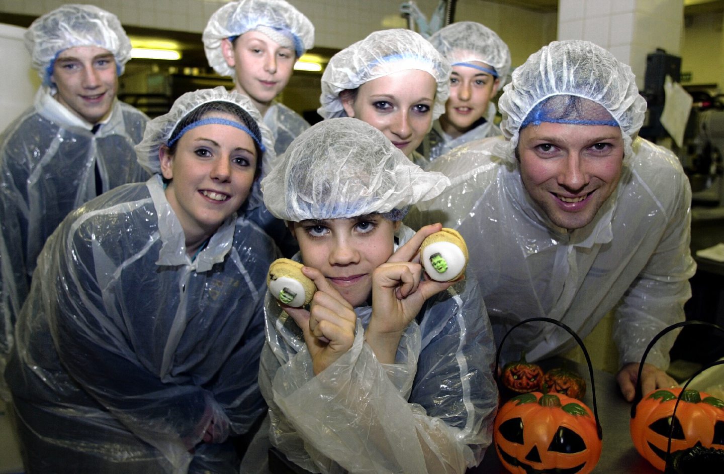 Inverurie Academy wearing plastic clothing covers and hair nets. One pupil at the front is holding Halloween-themed biscuits