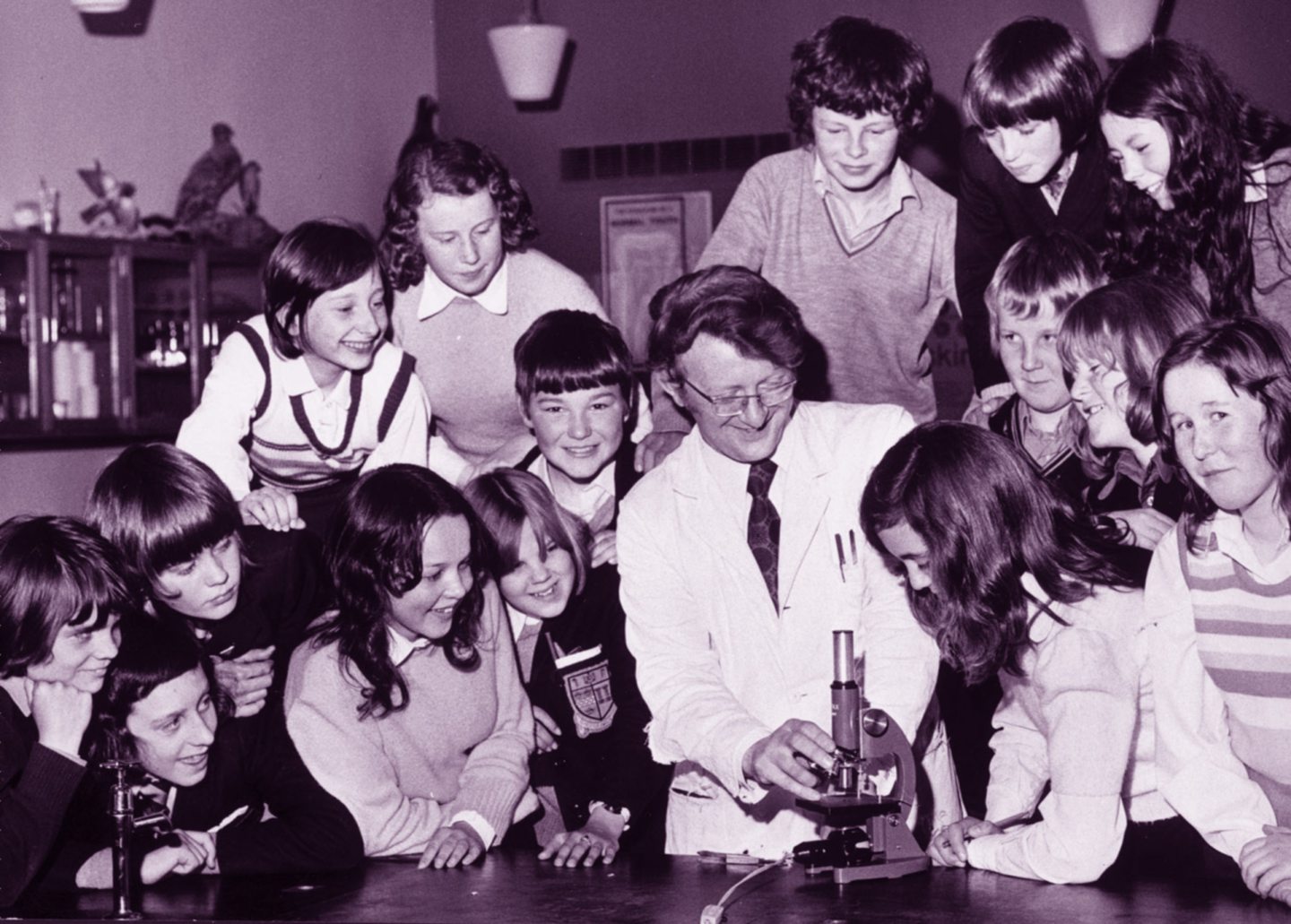 A biology teacher and his students gathered around a microscope