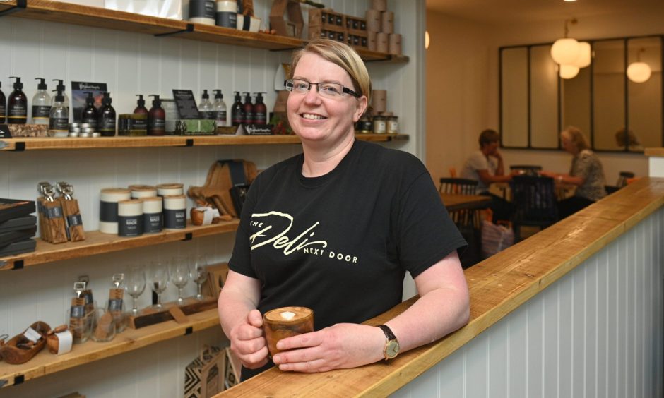 Faith Houlding smiling while sitting with cup of tea or coffee inside Deli Next Door.