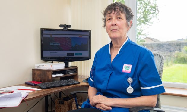 Carer Shona Scott in Moray Council uniform next to computer in her home.