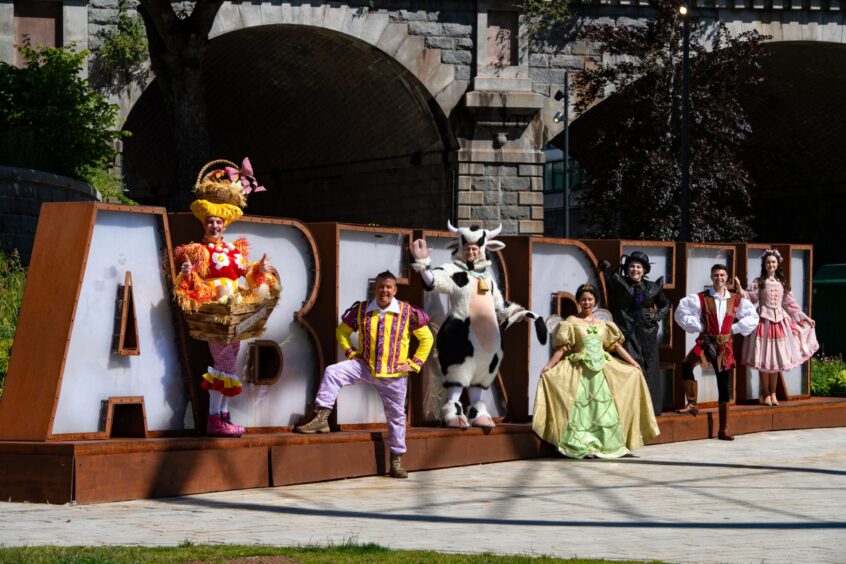 Aberdeen panto cast in front of Aberdeen sign at Union Terrace Gardens 