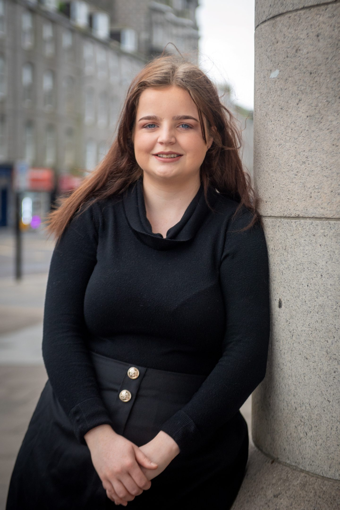 Sophie, dressed in black, smiles and looks at the camera while leaning on a pillar outside Aberdeen Sheriff Court