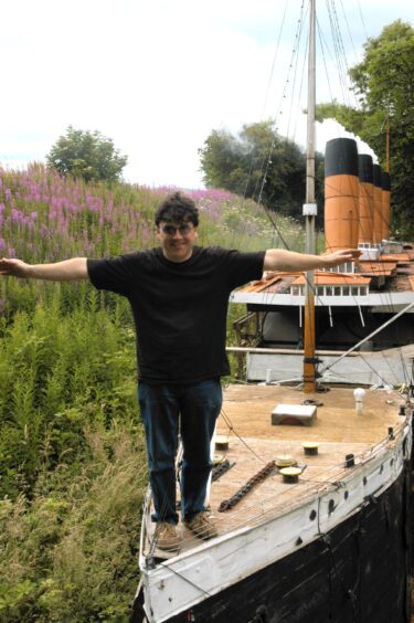 Stan on the bow of his Titanic replica, arms outstretched in the classic move pose.
