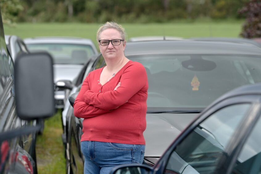 Michelle Clarke pictured in a red jumper and blue jeans beside her grey Vauxhall Astra.